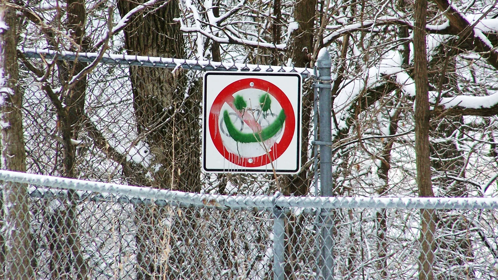 A chain-link fence with a sign, on which smiley face is painted