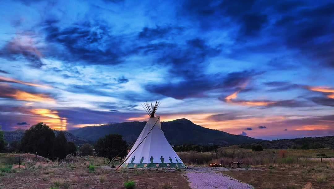 Lone teepee beneath vibrant sunset and distant mountains