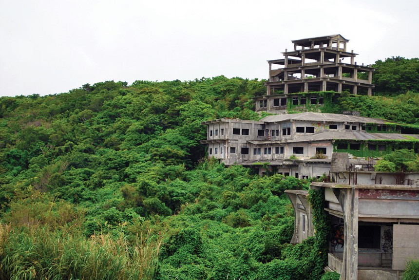 Abandoned concrete buildings overgrown by dense green jungle