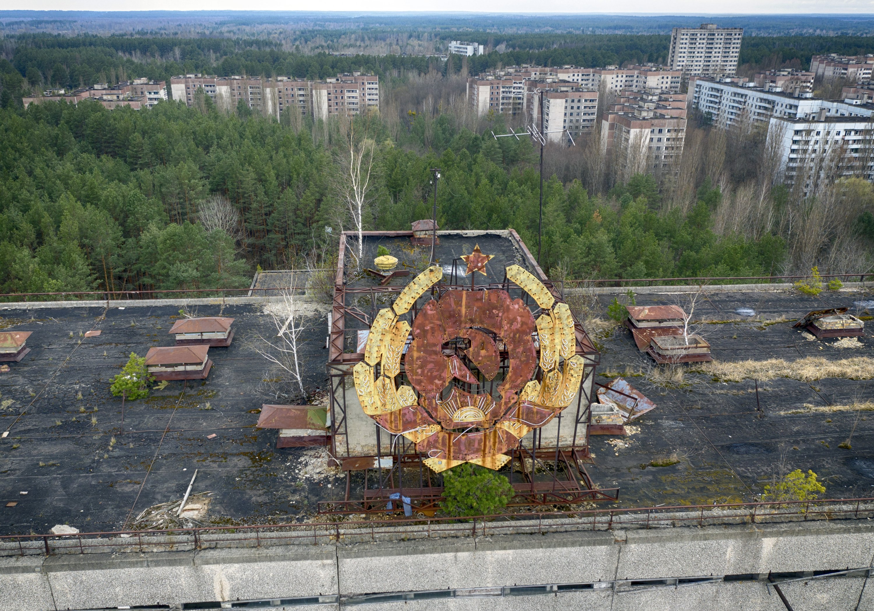 Rusting Soviet emblem atop abandoned rooftop overlooking forest